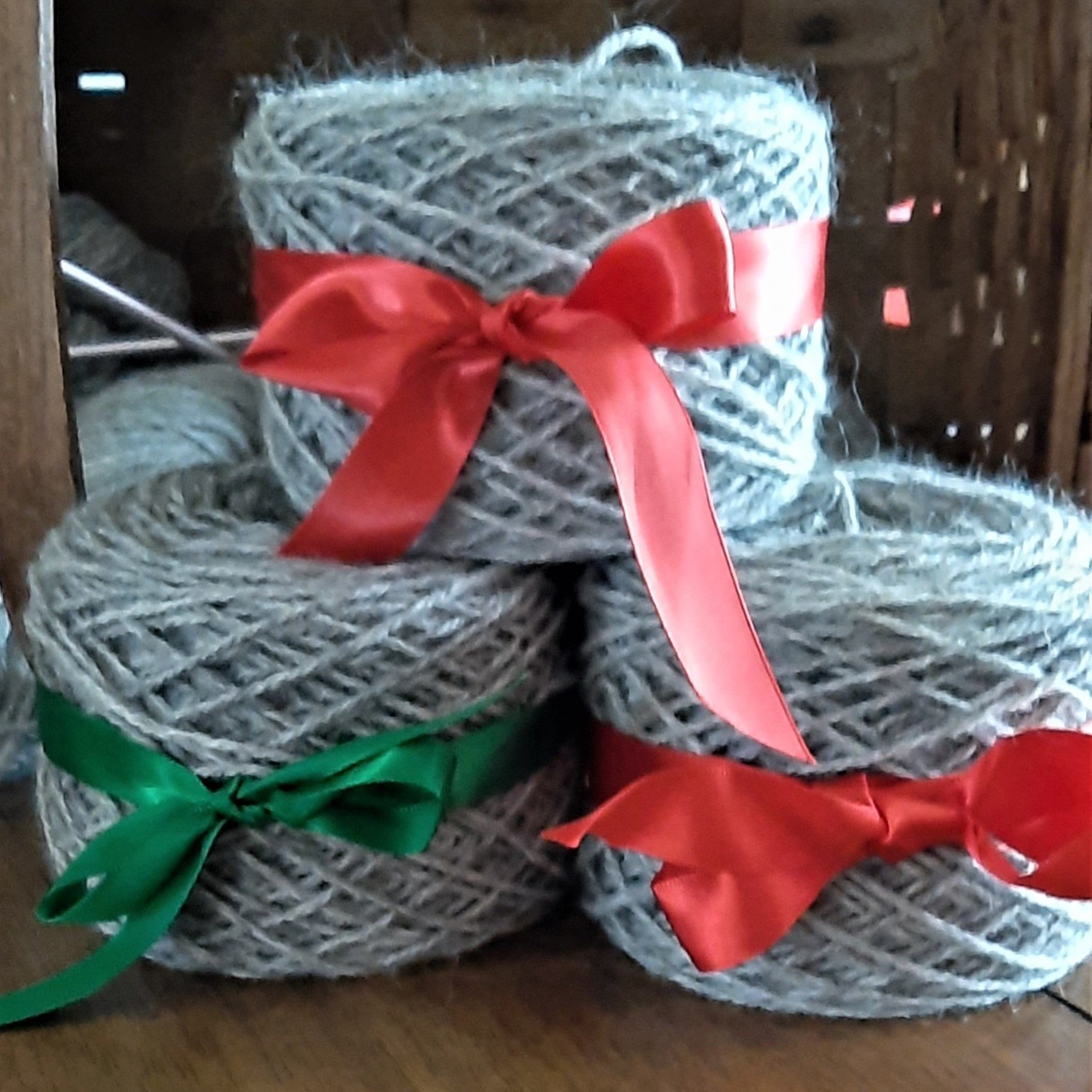 Barbara+Abend+-+yarncakes Three neatly arranged skeins of gray yarn tied with colorful ribbons, red and green, displayed on a wooden surface. Ideal for crafting, knitting, or DIY projects, showcasing a cozy and creative atmosphere.